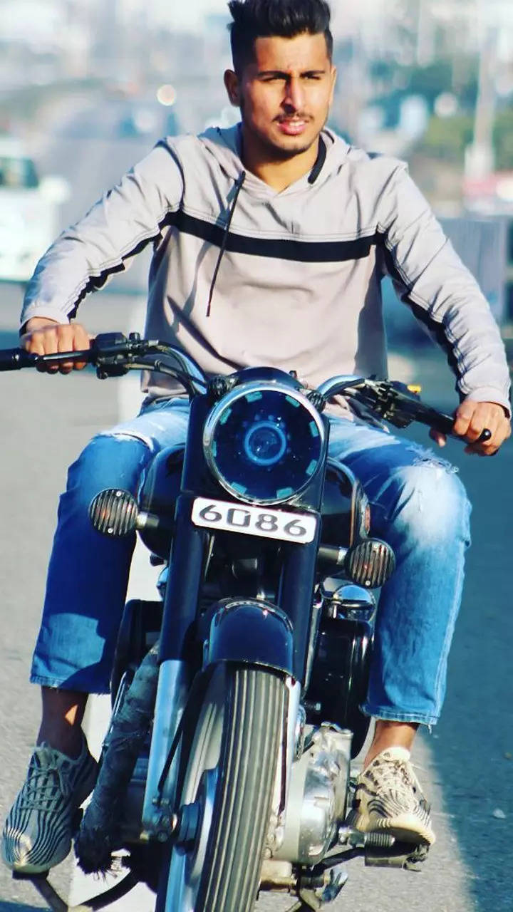 Full body of serious adult ethnic male biker in stylish outfit and helmet  sitting on haunches and checking broken motorbike details on road near lush  Stock Photo - Alamy