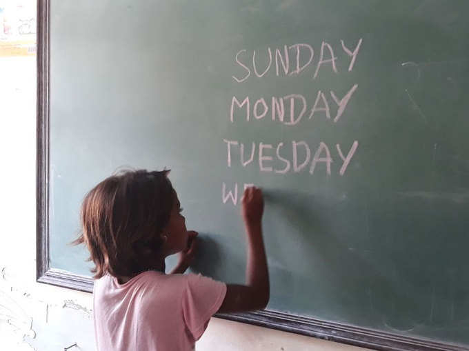 ब्लैक बोर्ड पर संडे-मंडे लिखती बच्ची