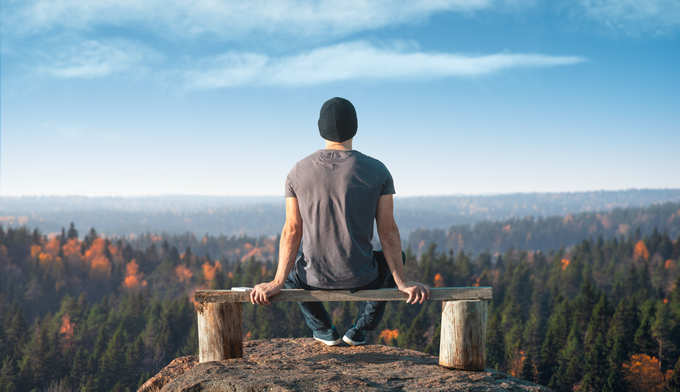 A man sits on a lookout point above the forest