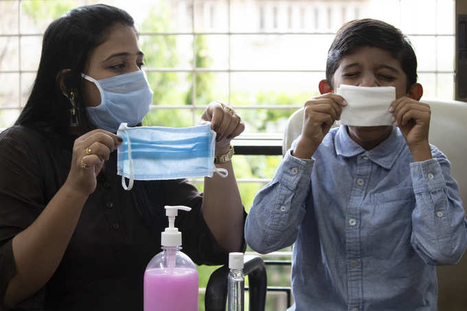 Cautious mother holding medical face mask for son Istock