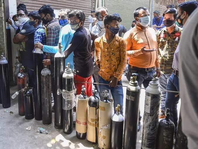 New Delhi_ Family members of COVID-19 patients wait outside an oxygen-filling ce....