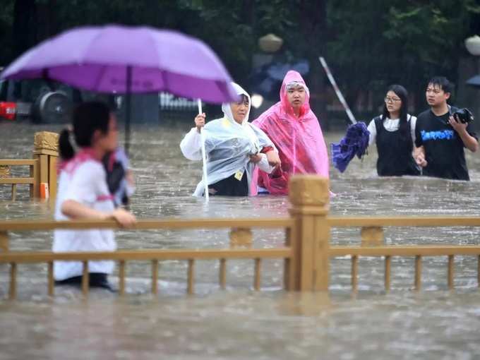 Zhengzhou _ People walk through floodwaters along a street in Zhengzhou in centr....