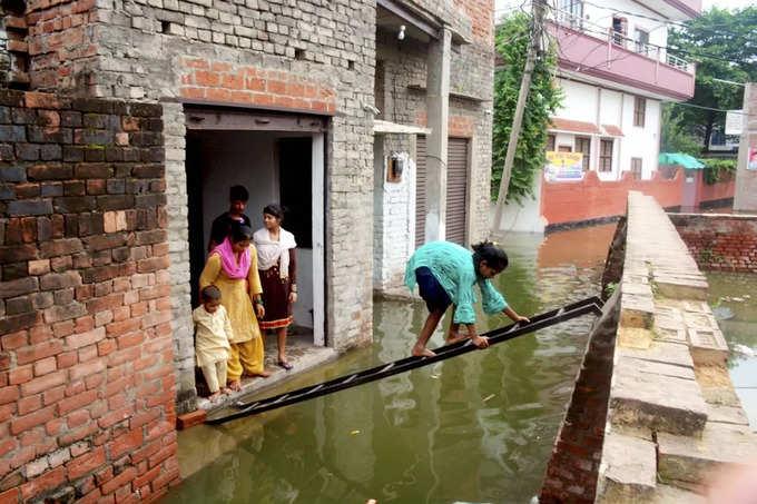 Varanasi: Residentials use a ladder to cross the flooded area after the water le...