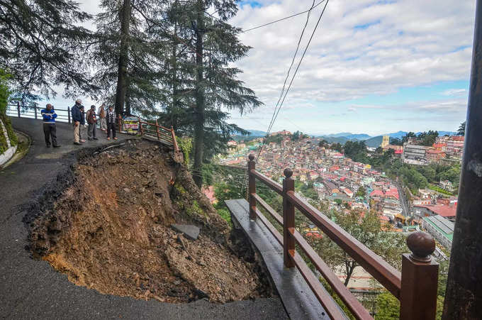 Shimla: Commuters stand near the caved-in portion of a road after heavy rainfall...