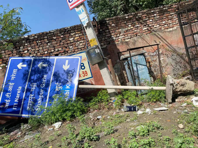 ​नरेला-अलीपुर रोड: कई महीने से गिरा पड़ा है साइन बोर्ड