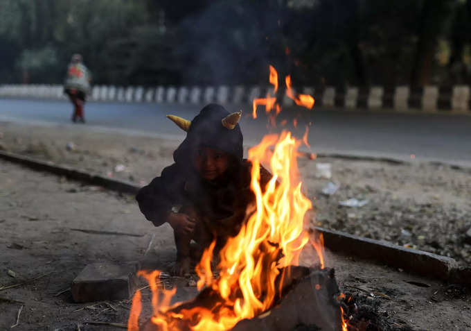 A child sits next to a campfire on a cold winter