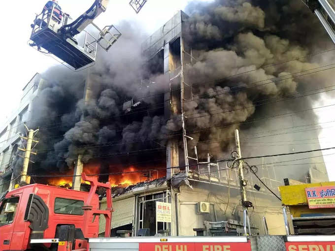 इमारत में आग लगने के बाद उठता भयानक धुंआ और पानी का छिड़कांव कर बुझाने का प्रयास करते दमकलकर्मी