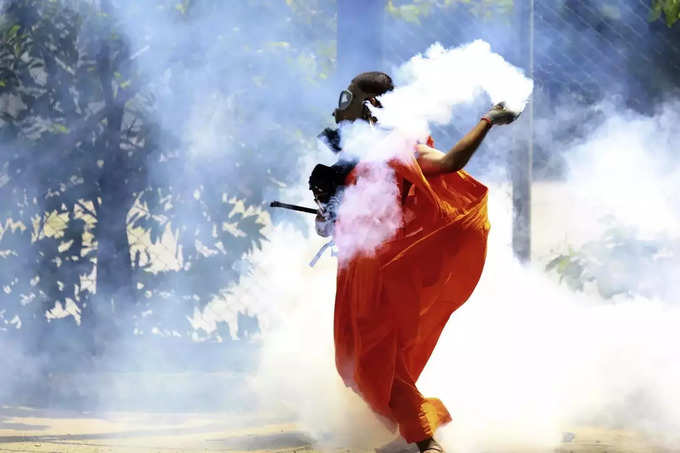 A man throws back a tear gas shell after it was fired by police to disperse the ....