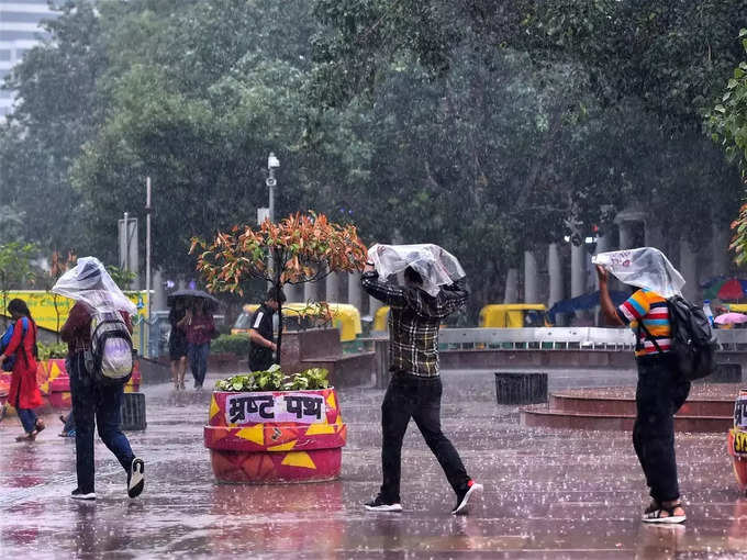 दिल्ली में तेज बारिश से बचने के लिए सिर को ढंककर बचने का प्रयास करते नौजवान