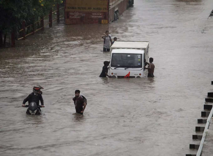 Gurugram: Commuters push their vehicle down the waterlogged Delhi-Gurugram Expre...