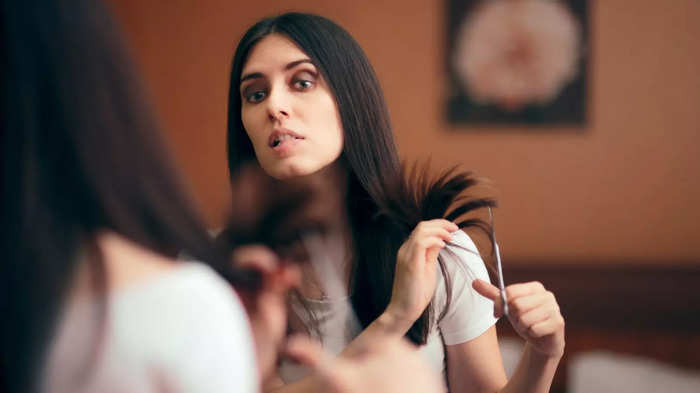 Woman Looking in Mirror Cutting Split Hair Ends stock photo