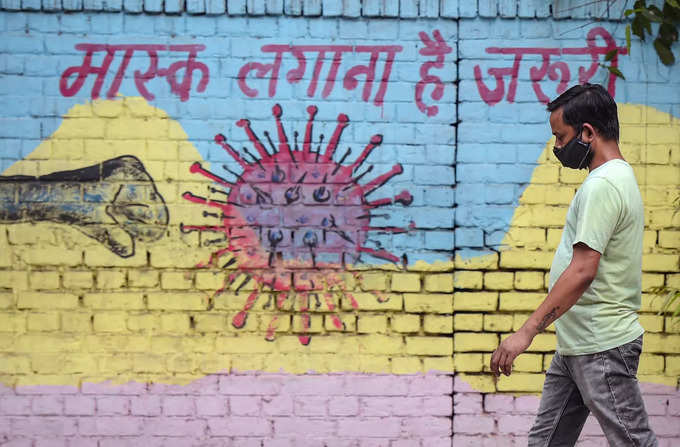 New Delhi: A man walks past a graffiti depicting coronavirus during the ongoing ...
