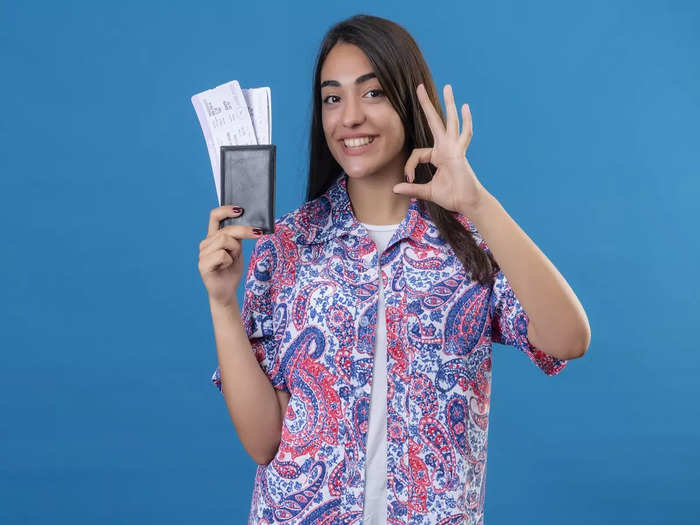 young-beautiful-woman-tourist-holding-passport-with-tickets-looking-camera-smiling-cheerfully-doing-ok-sign-standing-isolated-blue-background